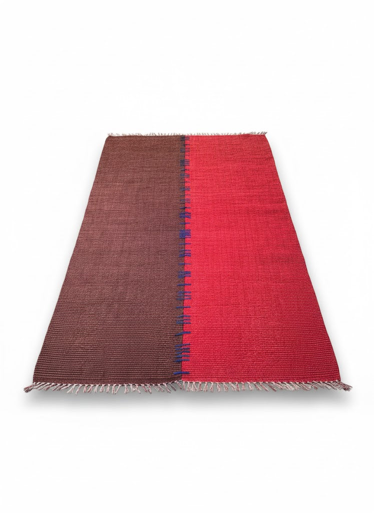 Tapis rectangulaire tissé plat, bicolore rouge vif et brun foncé, avec une démarcation centrale décorée de fines franges bleues. Dimensions $170 \times 240 \text{ cm}$